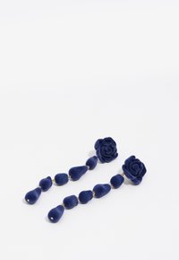 Pendientes de terciopelo azul marino con copas en forma de rosa y formas de lágrima colgantes, acentuados por elementos de metal dorado. Textura suave en toda su superficie.