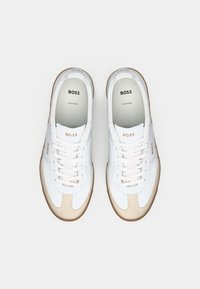 Vita sneakers med beige mockadetaljer, rund tå, platta snören, gummisula och logotillbehör på sidorna och tungan.