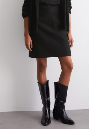 Black wool skirt with a straight cut, paired with shiny black leather knee-high boots featuring a pointed toe and chunky heel.