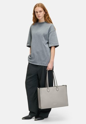 Szary, oversize T-shirt z miękkiego materiału, w połączeniu z luźnymi czarnymi spodniami. Trzymając usztywnioną szaro-torby tote z długimi uchwytami i minimalistycznym designem.