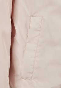 Tissu rose clair, lisse et avec un léger éclat ; présente une petite poche rectangulaire et des coutures soignées le long des bords.