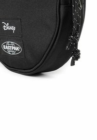 Borsa rotonda nera realizzata in tessuto resistente, con i loghi di Disney e Eastpak, dotata di chiusura con zip e dettagli con cordoncini annodati.