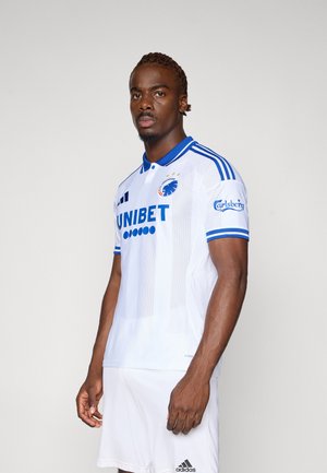 Hvid fodboldtrøje med blå krave og accenter, der har sponsorløb og holdmærke. Polyesterstof, slim fit design og korte ærmer.