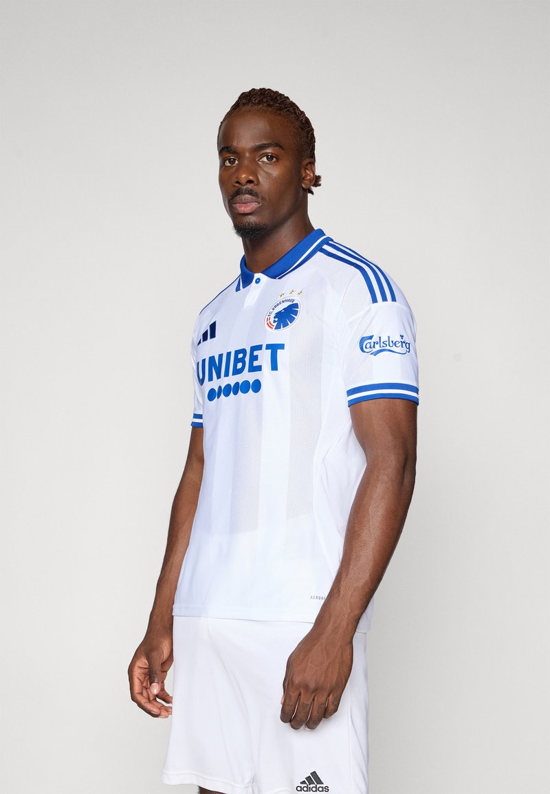 Hvid fodboldtrøje med blå krave og accenter, der har sponsorløb og holdmærke. Polyesterstof, slim fit design og korte ærmer.