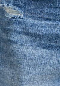 Närbild av blå denimtyg med en liten, fransig reva nära övre vänstra hörnet.