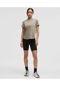 Light brown, short-sleeved t-shirt with a rounded hem, paired with black biker shorts. Footwear is white with black accents.