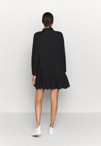Abito nero con maniche lunghe e orlo a balze. Realizzato in un tessuto leggero, il design presenta un colletto classico e una vestibilità comoda.