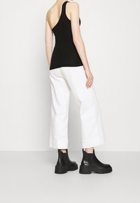Top aderente nero con design a spalla unica, abbinato a pantaloni bianchi larghi e stivali neri chunky alla caviglia.