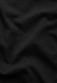 Tissu noir avec des plis doux et une texture fine tricotée créant des ombres et des reflets délicats.