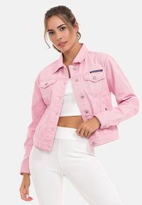 Roze denimjack met een klassieke snit, voorzien van zilveren knopen, borstzakken en een licht verweerde afwerking. Gecombineerd met een wit geribd top.