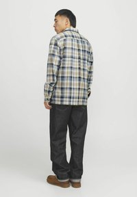 Beige, blaue und braune karierte Hemd mit Knöpfen, kombiniert mit dunkelblauer Jeans und braunen Schuhen, von hinten betrachtet.