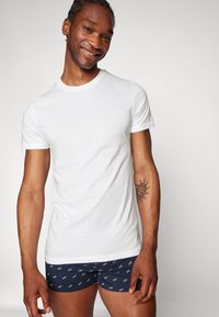T-shirt en coton blanc à col rond, associé à un short marine avec un motif répétitif du mot "DAD". Manches courtes, texture lisse.