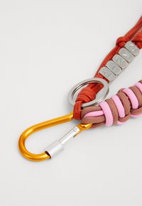 Accessory featuring a golden carabiner, braided in brown and pink paracord, with a silver circular ring and orange leather accents.
