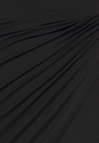 Mustaa kangasta, jossa on riippuvia laskoksia ja sileä rakenne, johon on ommeltu tasaisesti luoden kerroksellisen ulkonäön.