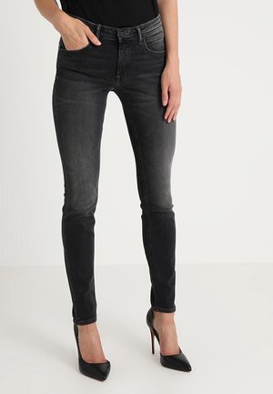 Jeans skinny negros de tela denim, con un lavado desgastado, estilo de cinco bolsillos y un ajuste ceñido. Combinados con zapatos de tacón alto negros.
