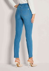 Blauwe skinny jeans van denim met een hoge taille, witte stiksels en achterzakken; gedragen met doorzichtige haksandalen. Gladde textuur.