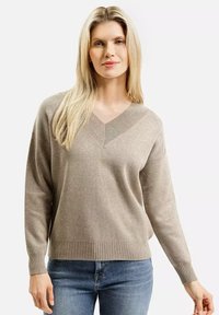 Beżowy sweter z dekoltem w serek, z długimi rękawami i prążkowanym dołem. Miękka faktura, luźny krój oraz subtelny wzór dzianiny wzdłuż dekoltu.