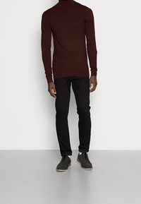 Maglione a collo alto marrone aderente abbinato a pantaloni neri slim-fit e scarpe nere con lacci grigio scuro e suola marrone chiaro.