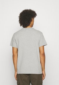 Tricou gri din bumbac, cu mâneci scurte, guler rotund și o croială lejeră. Țesătura pare netedă, cu o textură moale.