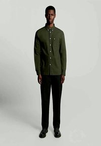 Cămașă verde cu guler, buzunar pe piept și butoane albe, asociată cu pantaloni negri și pantofi negri. Design simplu, ajustat.