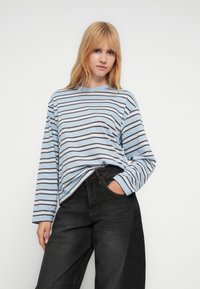 Μπλούζα με μακριά μανίκια και στρογγυλή λαιμόκοψη σε ανοιχτό μπλε χρώμα με οριζόντιες ρίγες σε σκούρο μπλε και καφέ. Συνδυασμένη με μαύρο παντελόνι φαρδιάς γραμμής.