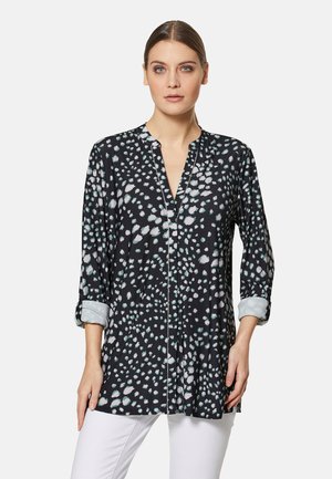 Schwarze Bluse mit hellblauen und weißen Punkten, mit Kragen und langen Ärmeln, die an den Bündchen hochgerollt sind, in einem lockeren, fließenden Design.