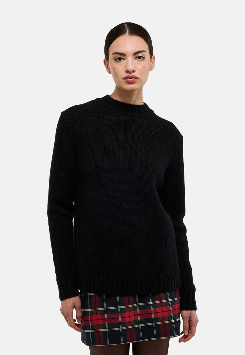 Pull en tricot noir avec un col rond, des poignets et un ourlet côtelés. Associé à une jupe à carreaux aux couleurs rouge, vert et marine.