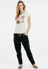 Lichtbeige t-shirt met korte mouwen en tropische print, gecombineerd met zwarte tapered cargo pants met zakken en omgeslagen onderkanten.