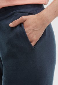 Navy Sweatpants mit weicher Textur und seitlichem Taschen, ausgestattet mit einem bequemen elastischen Bund und einer Nahaufnahme einer Hand in der Tasche.