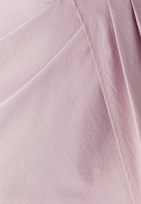 Lichtroze stof, gladde textuur, met een subtiele glans en gevouwen plooien. Zichtbare stiksels voegen details toe aan het oppervlak van het materiaal.