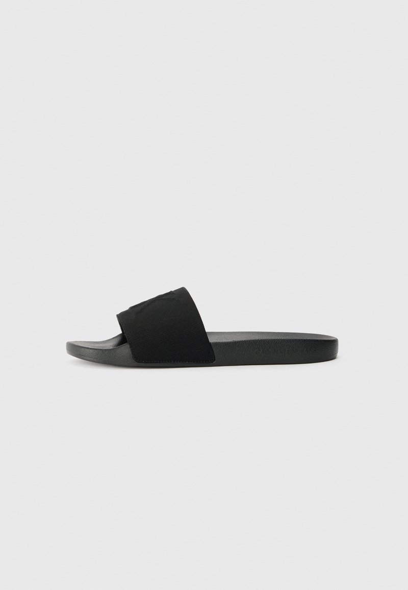 Black slide sandal featuring a textured fabric upper, flat rubber sole, and minimalistic design. No visible logos or hardware details.