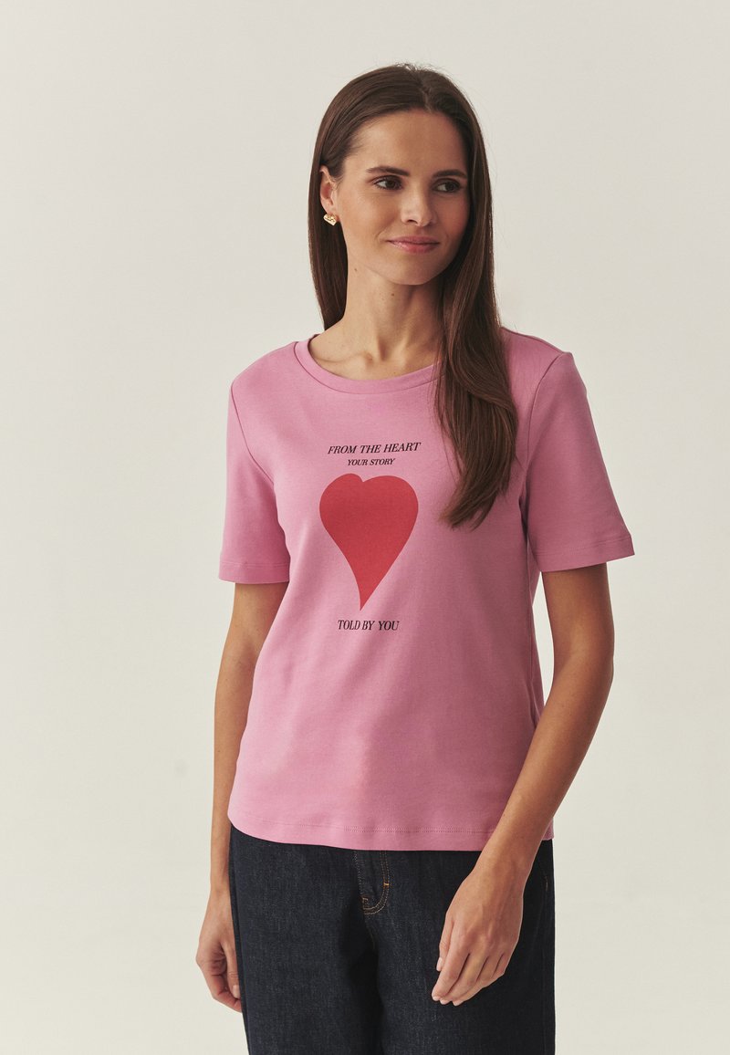 T-shirt en coton rose à manches courtes, col rond, avec un motif de cœur rouge et le texte : « FROM THE HEART YOUR STORY TOLD BY YOU. »