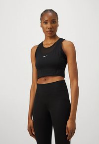 Black sports crop top with mesh neckline and Nike logo, paired with black high-waisted leggings. Smooth texture and fitted design.