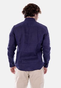 Camicia a maniche lunghe in lino viola scuro, con colletto rifinito, polsini con bottoni e orlo dritto con due pieghe posteriori.