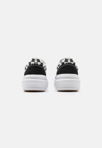 Baskets à motif damier noir et blanc avec un talon en daim, semelle en caoutchouc blanche et détails en couture. Vue arrière mettant en avant les détails du design.