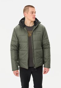 Groene pufferjas met een zwarte capuchon en ritssluiting, met een gequiltde textuur, twee voorzakken en een subtiel logo op de borst.