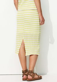 Jupe midi en tricot avec des rayures blanches et jaunes, comportant une fente sur le côté. Associée à des sandales brunes avec imprimé léopard et boucles.