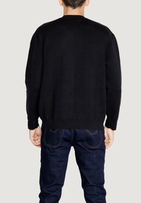 Maglione nero a maglia con un motivo texturizzato, scollatura rotonda, vestibilità rilassata e maniche lunghe, abbinato a jeans in denim scuro.