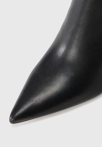 Black pointed-toe pump made of smooth leather. Features a sleek silhouette with a glossy finish and a textured surface.