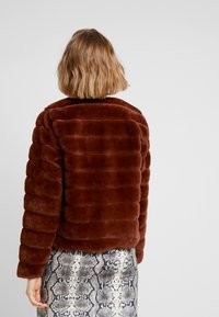 Veste en fausse fourrure marron à rayures horizontales et col rond, associée à une jupe imprimée serpent, avec une texture douce et un design moelleux.