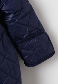 Manica di giacca trapuntata blu navy, con texture simile alla seta, polsini a coste e motivo a rombi cucito per l'isolamento.
