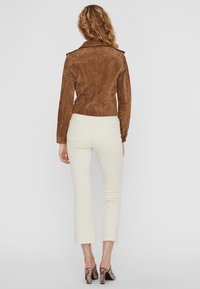 Bordeaux suède jack met schoudertabs, nauwsluitend ontwerp, lichtgewicht textuur, gecombineerd met lichtbeige cropped jeans en slangenprint hakken.