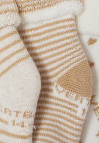Nahaufnahme von beigen und weißen gestreiften Stricksocken mit strukturierten Bündchen und kleiner bedruckter Schrift auf der Sohle.
