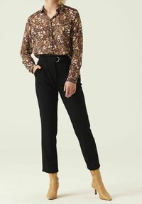 Camicia a fiori con bottoni in tonalità viola e gialle, abbinata a pantaloni neri a vita alta e stivaletti beige con tacco.