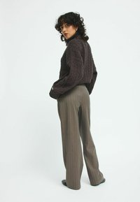 Pull en maille torsadée marron foncé avec col montant, associé à un pantalon large gris à rayures. Textures douces et coupe ample.