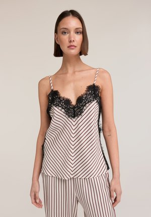 Jonge vrouw met kort bruin haar, gekleed in een gestreepte witte en bordeauxkleurige mouwloze top met zwarte kanten rand en bijpassende gestreepte broek.