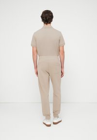 Μπεζ βαμβακερό πόλο πουκάμισο με κοντά μανίκια, σετ με αντίστοιχο στενό παντελόνι φόρμας. Διαθέτει πίσω τσέπη και ελαστική μέση.