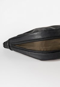 Schwarze Lederhandtasche mit strukturierten Oberflächen, ausgestattet mit einem auffälligen Reißverschluss und einem Netzfutter für innere Sichtbarkeit. Schlanker, schräger Schnitt.