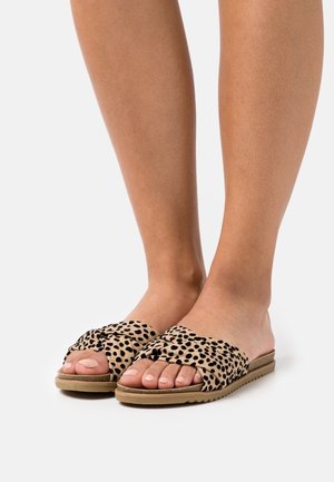 Sandalias planas tipo slide beige con lunares negros, que presentan una correa de tela torcida y una suela flexible, mostrando los dedos expuestos y un perfil plano.