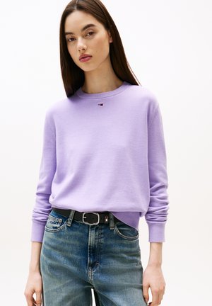 Maglione lavanda con maniche lunghe e scollatura rotonda, realizzato in un materiale morbido. Abbinato a jeans blu a vita alta e una cintura nera.